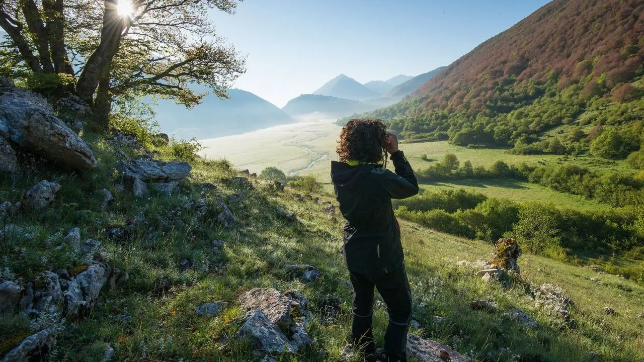 A person overlooks a sunlit mountain valley in Italy.